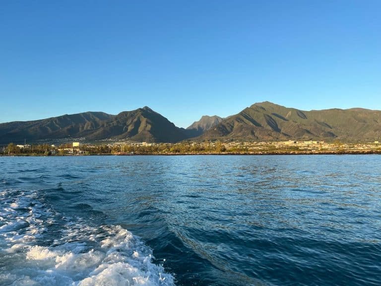 A scenic view of a mountain range under a clear blue sky, seen from a body of water with rippling waves, during daylight.