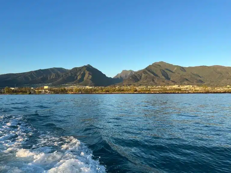 A scenic view of a mountain range under a clear blue sky, seen from a body of water with rippling waves, during daylight.