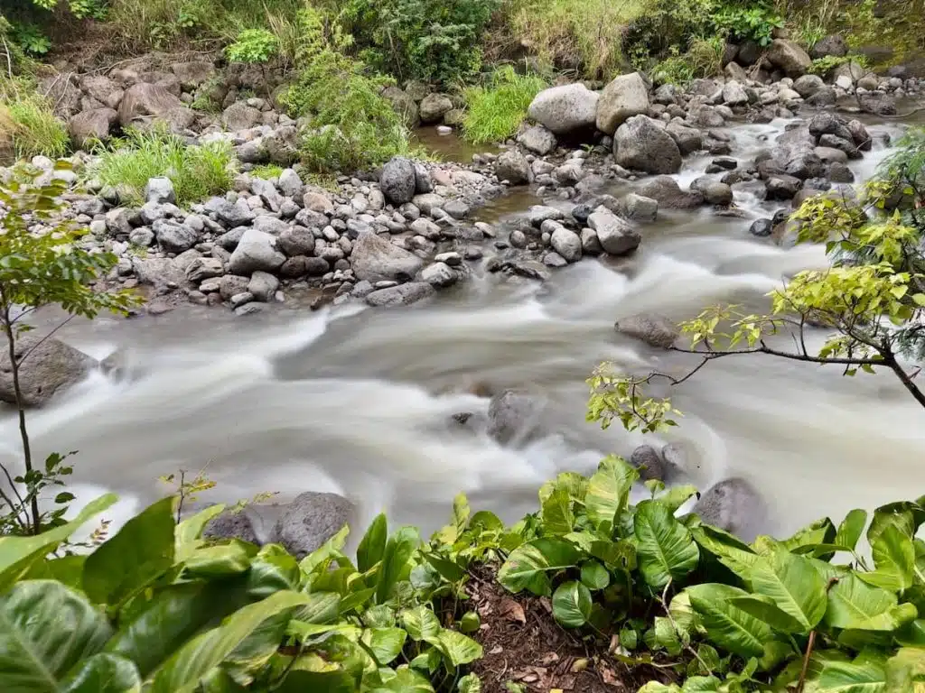 A flowing river with silky smooth water surrounded by rocks and lush greenery, creating a serene natural landscape.