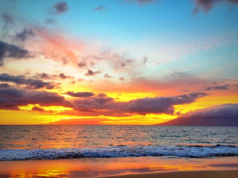 A vibrant sunset over the ocean, with the sky painted in shades of orange, pink, and blue, and gentle waves lapping against the sandy shore.