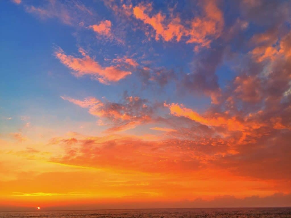 A vibrant sunset over the ocean with a sky filled with shades of orange, pink, and blue clouds.