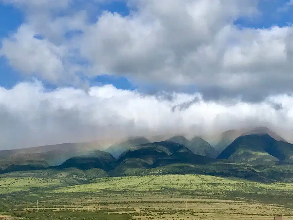 A scenic view of green hills under a cloudy sky, with a faint rainbow visible above the hills.