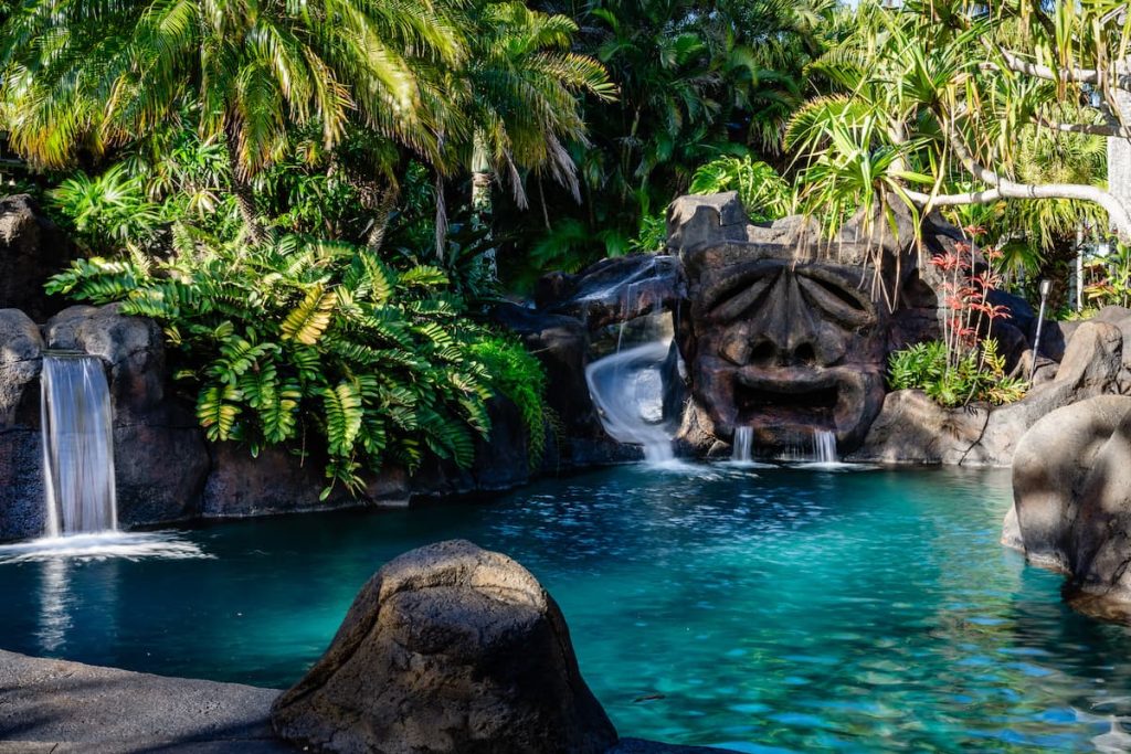 The pool area at 1780 Kauhikoa Road includes a tiki head jumping rock, waterslide, oversized hot tub, lush landscaping and waterfalls. 