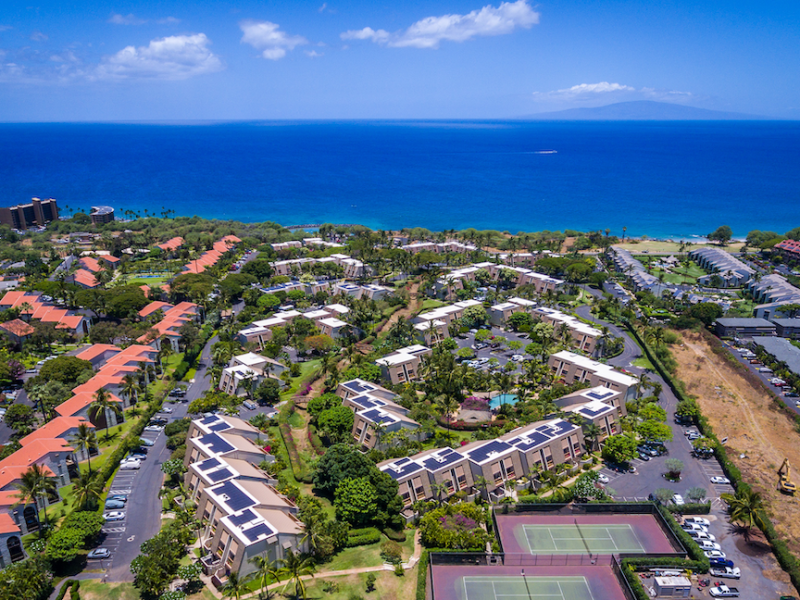 Aerial image showing multiple condo developments in South Kihei including four impacted by Bill 9. The shot looks over the buildings to the bright Blue of the Pacific Ocean with the Island of Lanai towards the horizon. Maui Hill, on the left side of the photo, is one of the developments included in County Council sponsored resolutions to change the properties to H3/H4 zoning.