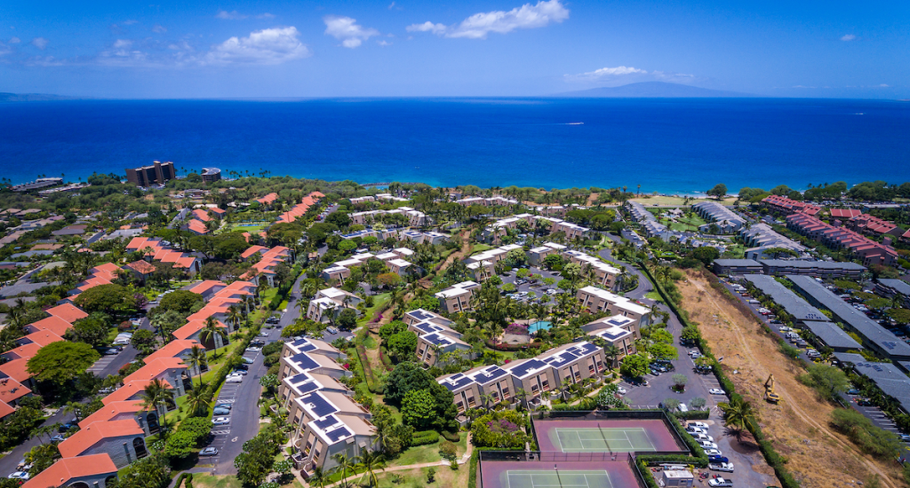Aerial image showing multiple condo developments in South Kihei including four impacted by Bill 9. The shot looks over the buildings to the bright Blue of the Pacific Ocean with the Island of Lanai towards the horizon. Maui Hill, on the left side of the photo, is one of the developments included in County Council sponsored resolutions to change the properties to H3/H4 zoning.